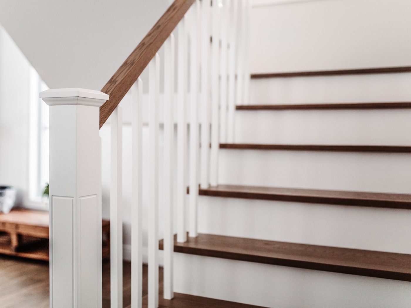 Un escalier blanc à marches et main courante de bois, barreaux blancs, lumière du matin