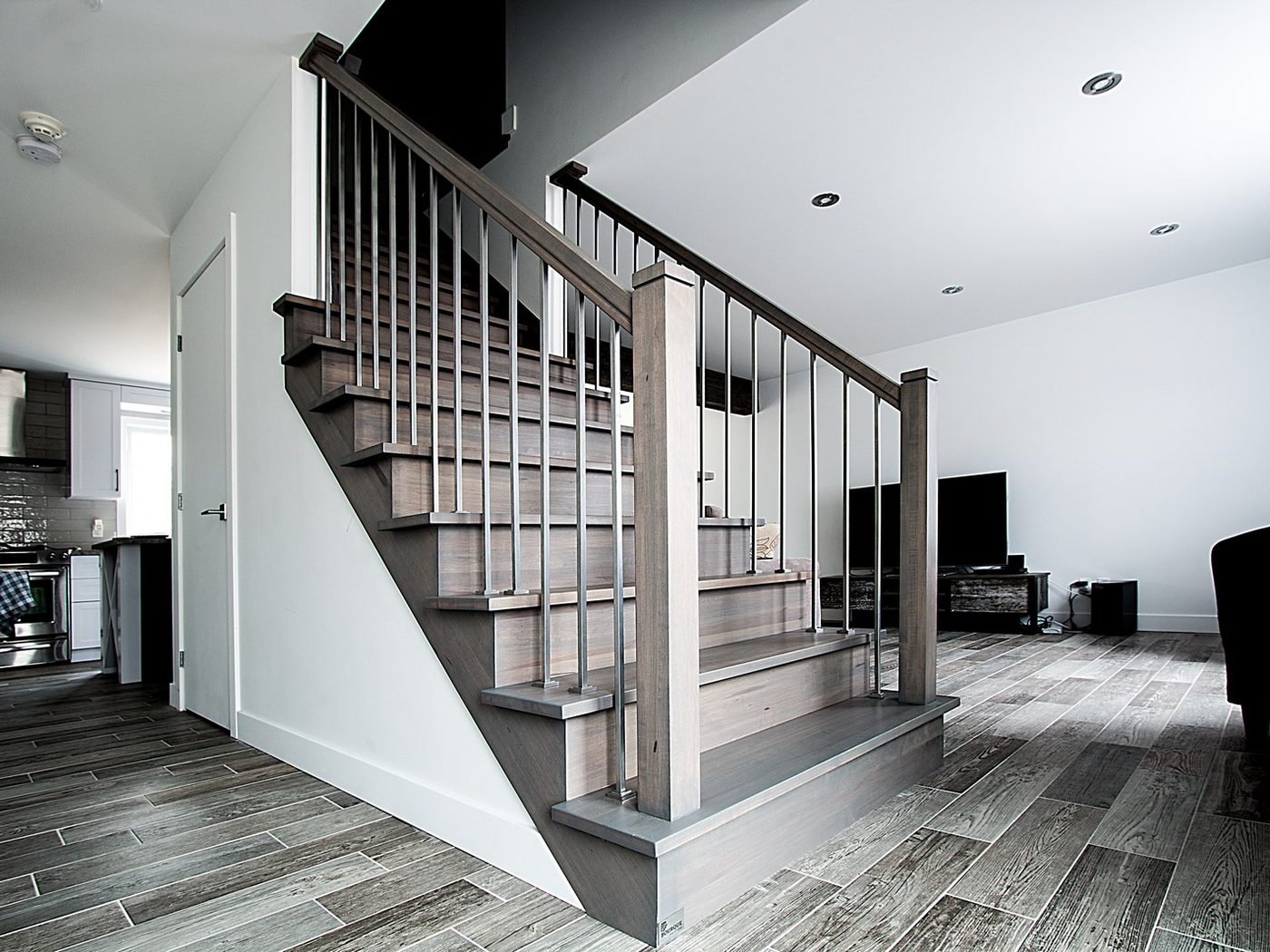 Un escalier d'érable teint gris aux barreaux d'acier, ouvert sur le salon et la cuisine