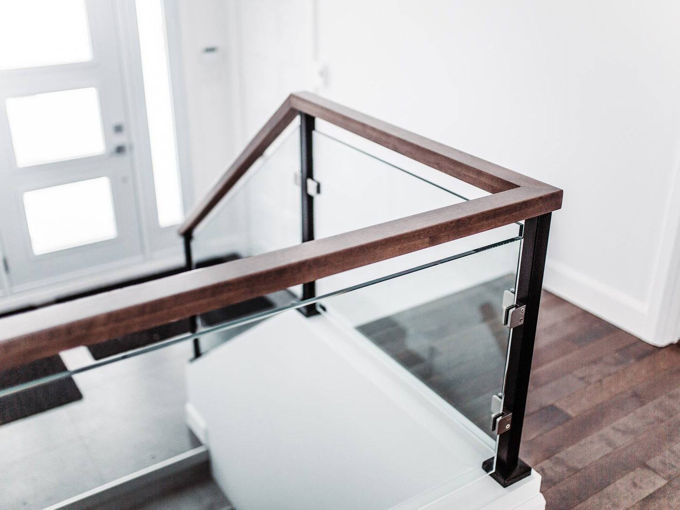 Une rampe de bois foncé à panneaux de verre autour d'une cage d'escalier, porte d'entrée vitrée