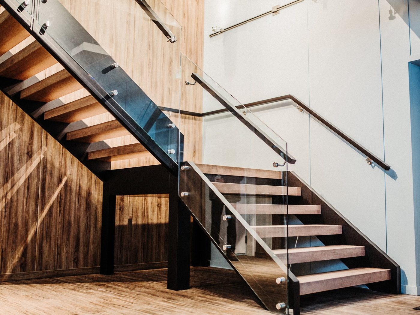 Un escalier de bois à garde-corps de verre le long d'un mur lambrissé de bois brut