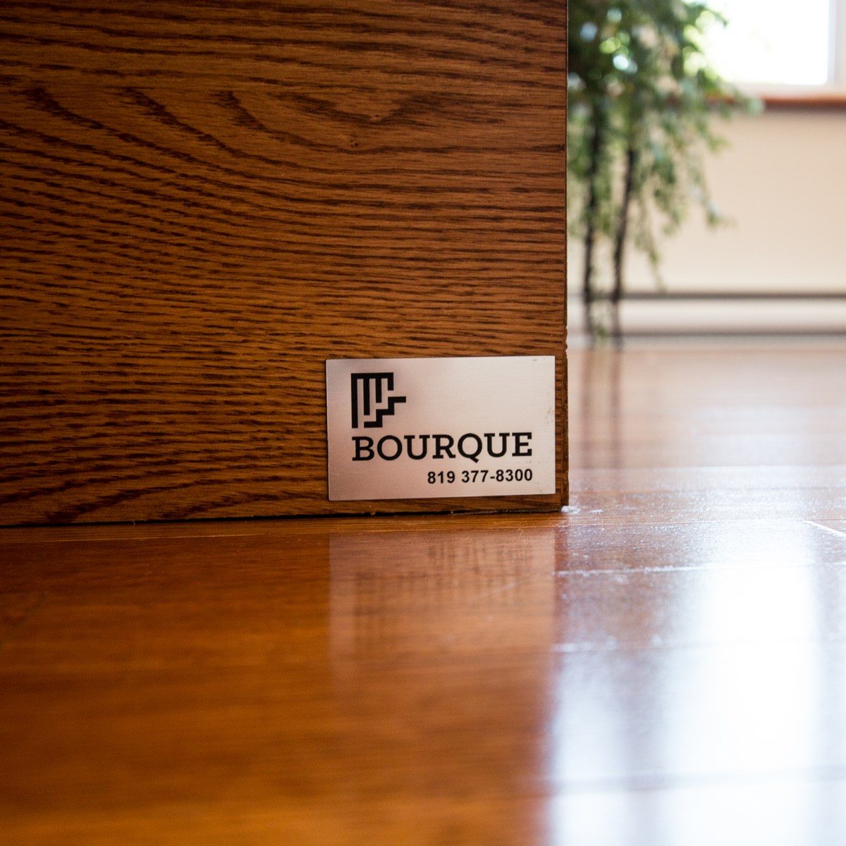 La plaque de métal Bourque, avec le numéro de téléphone, vissée sur le limon de chêne d'un escalier